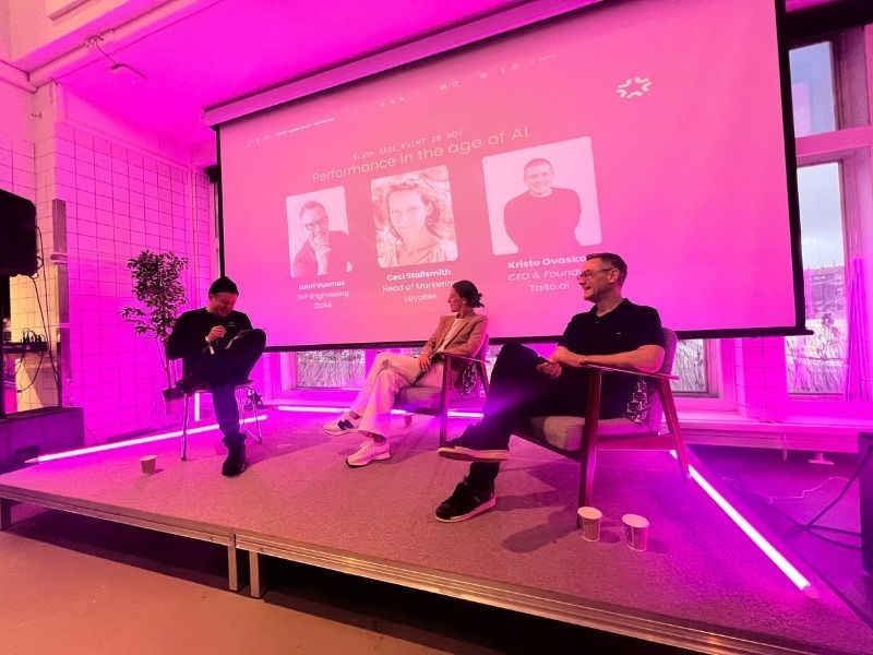 Kristo Ovaska moderating a live panel discussion with Ceci Stallsmith and Lauri Vuornos on stage at Maria01, with a projected screen behind them reading “Performance in the age of AI – A Slush side event featuring Lovable and ŌURA.”