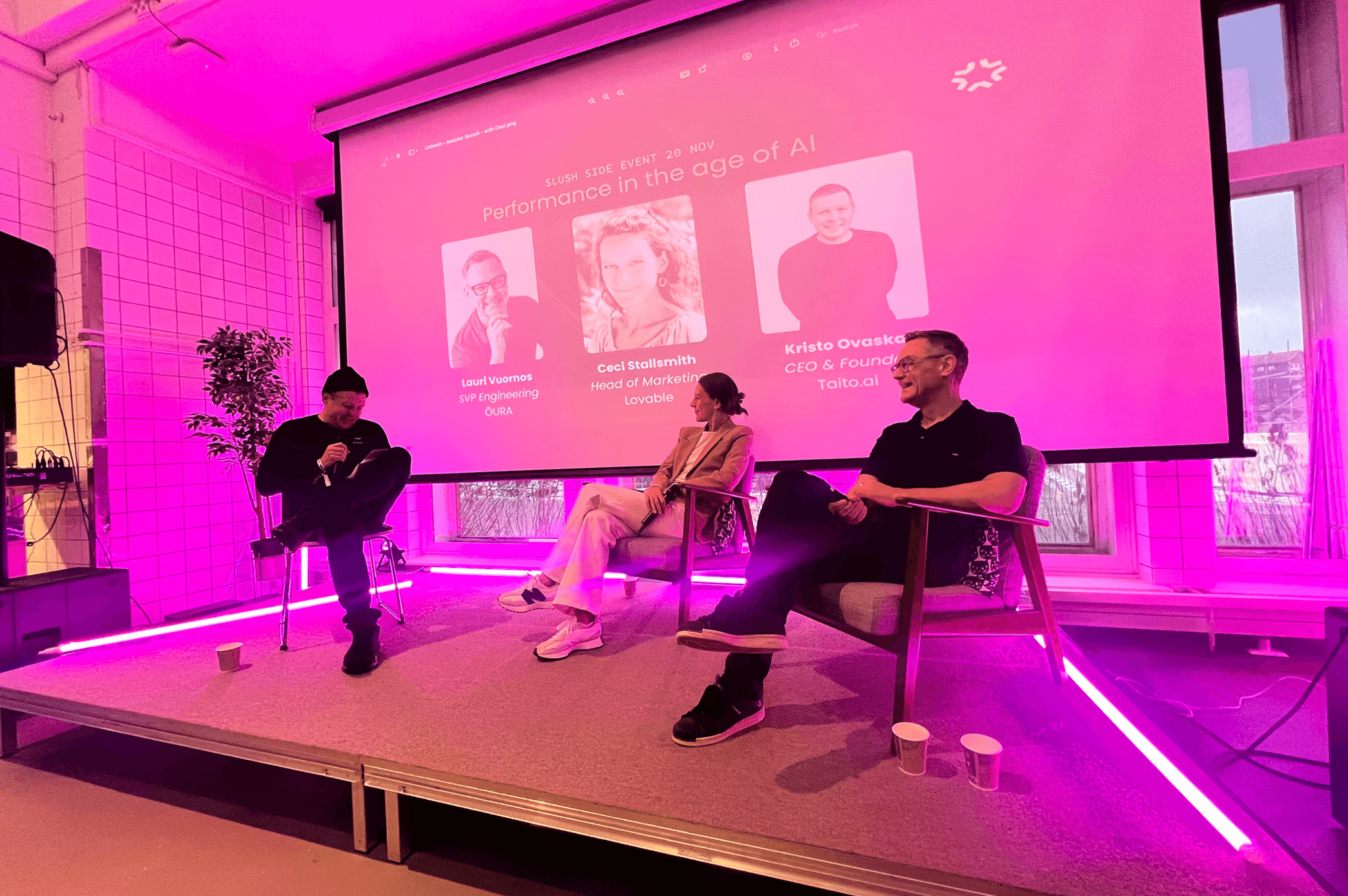 Kristo Ovaska moderating a live panel discussion with Ceci Stallsmith and Lauri Vuornos on stage at Maria01, with a projected screen behind them reading “Performance in the age of AI – A Slush side event featuring Lovable and ŌURA.”
