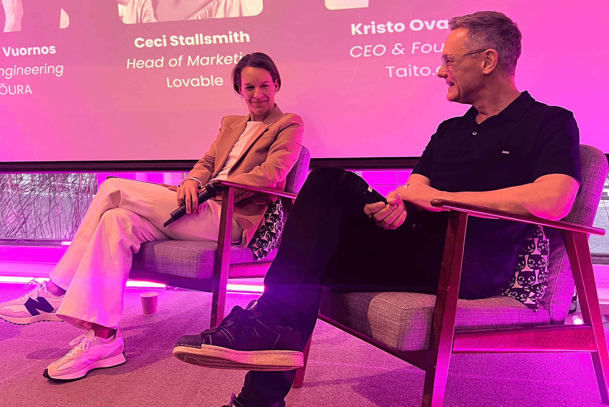 Two panelists seated on stage during a discussion on performance in the age of AI, with a presentation slide visible behind them and pink stage lighting at a Slush side event setting.